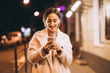 Mulher sorri mexendo no celular enquanto caminha na rua