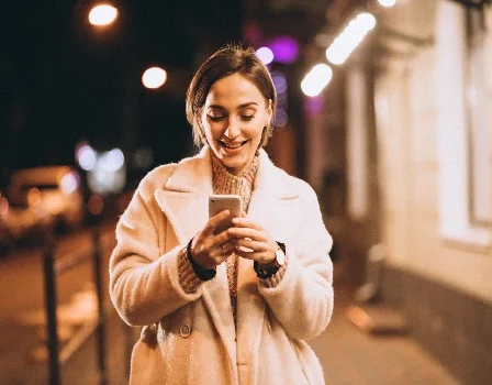 Mulher sorri mexendo no celular enquanto caminha na rua